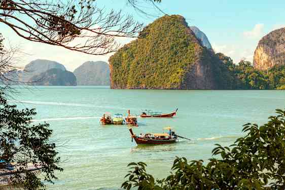 Pitkiä puuveneitä liikkuu vedessä, taustalla vihreitä vuoria. (Tekoälyn luoma teksti)