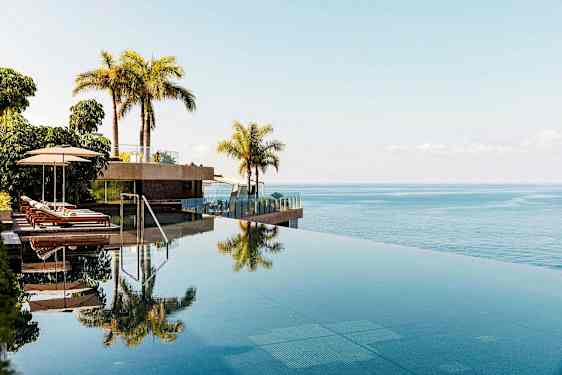 Infinity-allas aurinkotuoleilla ja palmuilla, näkymä merelle. (Tekoälyn luoma teksti)