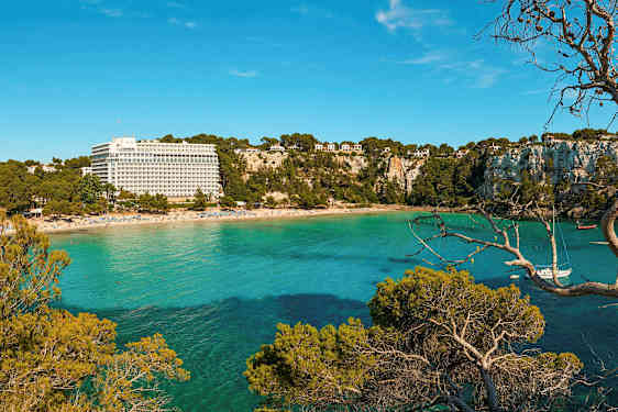 Ranta, jolla on lomakeskusrakennus ja vehreitä kallioita turkoosinsinisen meren äärellä. (Tekoälyn luoma teksti)