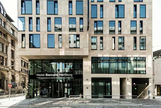 Rakennus, jossa on moderni julkisivu ja sisäänkäynti, jonka yläpuolella lukee "Hotel Barceló Hamburg". (Tekoälyn luoma teksti)