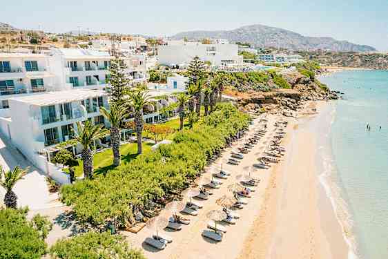 Ranta aurinkotuoleilla ja varjoilla hotellirakennuksen vieressä viheralueiden ympäröimänä. (Tekoälyn luoma teksti)