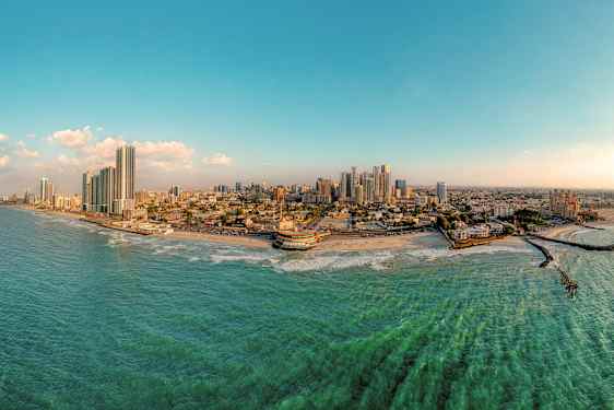 Panoraamakuva rannikkokaupungista, jossa on korkeita rakennuksia, ranta ja meri. (Tekoälyn luoma teksti)