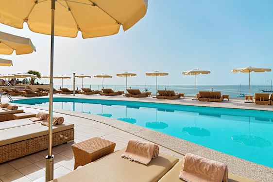 Aurinkotuoleja ja päivänvarjoja uima-altaan ympärillä, näkymä merelle. (Tekoälyn luoma teksti)