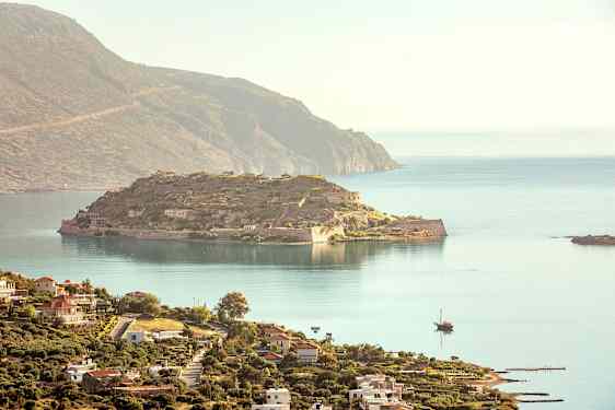 Näkymä historialliselle saarelle, jossa on raunioita ja ympäröivää merta, etualalla rannikkokaupunki rakennuksineen. (Tekoälyn luoma teksti)