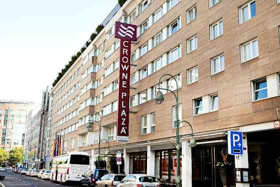 Crowne Plaza -hotellirakennus, jossa pysäköintimerkki ja bussi edessä. (Tekoälyn luoma teksti)