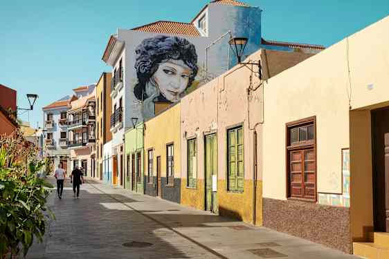 Värikkäitä talojen julkisivuja kävelytien varrella, jossa kaksi henkilöä kävelee. (Tekoälyn luoma teksti)