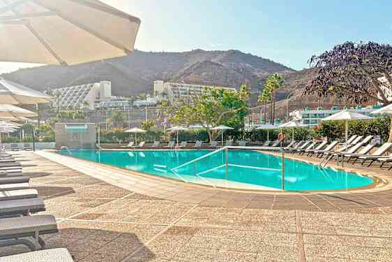 Ulkouima-allas, jossa on aurinkotuoleja ja sateenvarjoja, ympäröi vehreys ja vuoret. (Tekoälyn luoma teksti)