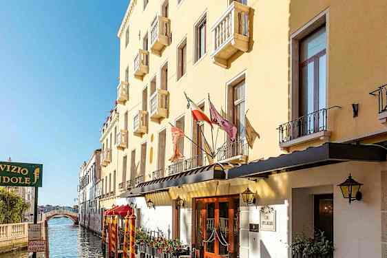 Keltainen rakennus, jossa on parvekkeita kanavan varrella, ja taustalla kävelysilta. (Tekoälyn luoma teksti)