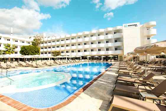 Ulkouima-allas, jota ympäröivät aurinkotuolit ja aurinkovarjot, taustalla monikerroksinen hotelli. (Tekoälyn luoma teksti)