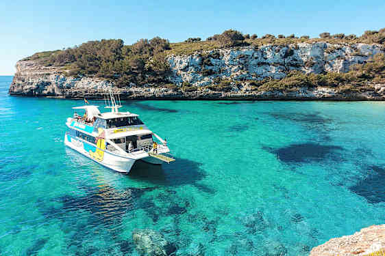 Valkoinen vene matkustajineen turkoosinsinisessä lahdessa, jota ympäröivät kalliot ja vehreys. (Tekoälyn luoma teksti)