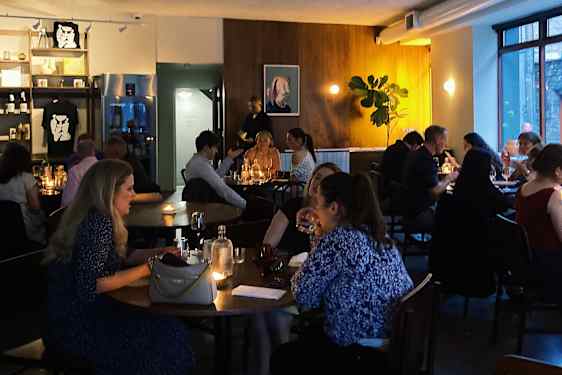 Ihmiset istuvat pöydissä ravintolassa, jossa on hillitty valaistus.