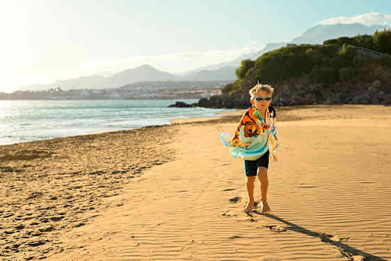Pieni poika juoksee uimaleluja kantaen hiekkarannalla
