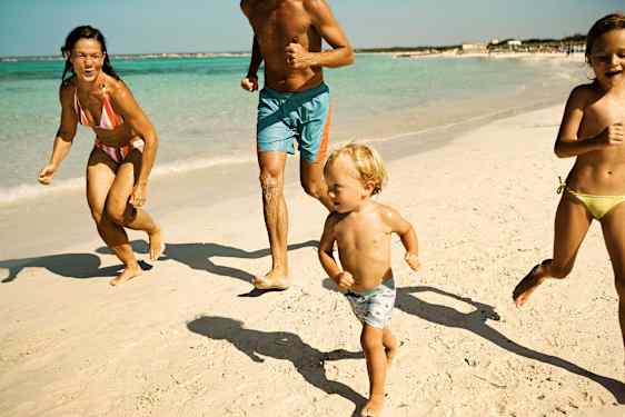 Lapsiperhe juoksee rannalla pakettimatkalla