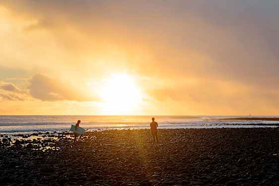 Surfare på strand i solnedgång