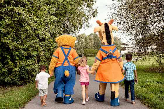 Lollo & Bernie kävelevät puistossa käsi kädessä kolmen lapsen kanssa. Kuva on otettu takaapäin.