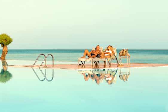 Ett par ligger i solstolar vid en infinitypool, med havet i bakgrunden