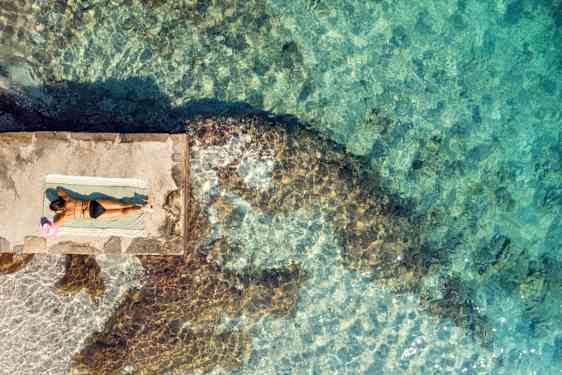 Nainen ottammassa aurinkoa meren äärellä