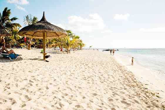 Perhe kävelee käsi kädessä hiekkarannan vesirajassa