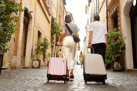 Mies ja nainen vetävät matkalukkujaan Rooman kadulla