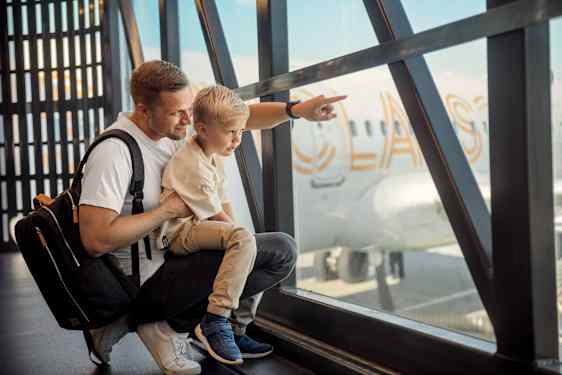 Isä ja lapsi katsovat lentokentälla ulos ikkunoista