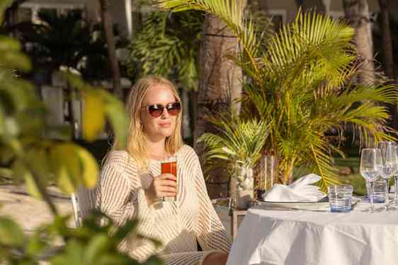 Nainen juoma kädessä, palmujen ympäröimänä