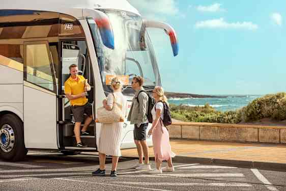 Kolme henkilöä tapaa matkaoppaan bussin ovella.