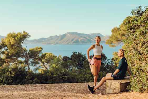 Nainen venyttelemässä, mies istuu penkillä