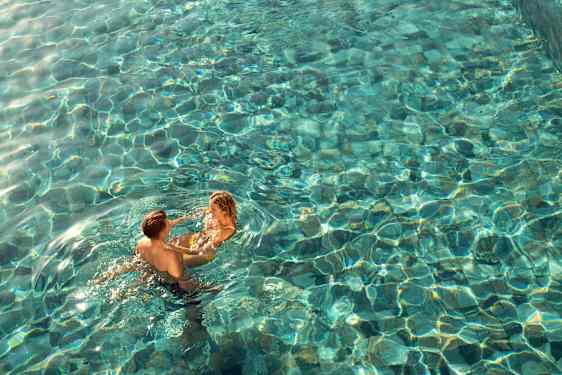 tarjoilija tuo samppanjalasillisen pöytään, jonka taustalla valkoinen hiekkaranta ja turkoosi meri