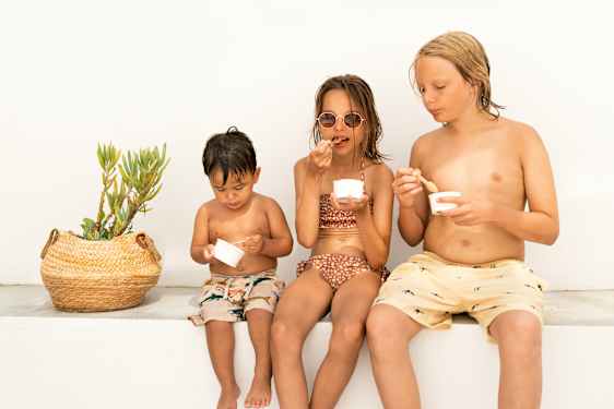 Kolme lasta vierekkäin syömässä jäätelöä pikareista