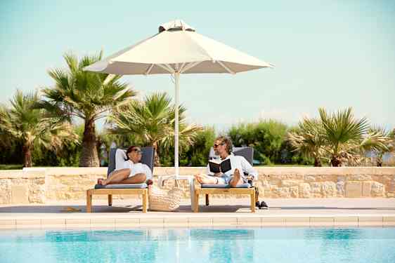 Pariskunta aurinkotuoleilla uima-altaalla