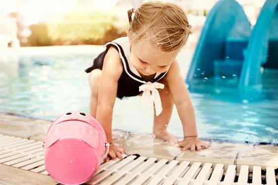 Pieni tyttö leikkii ämpärin kanssa uima-altaan reunalla