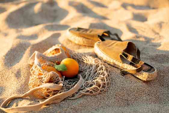 kengät, rantakassi ja appelsiini hiekalla