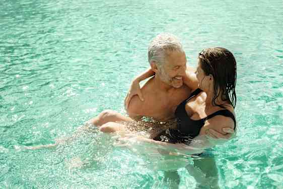Mies pitää naista sylissä uima-altaassa