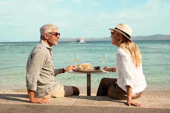 Mies ja nainen istumassa pöydän ääressä, taustalla meri