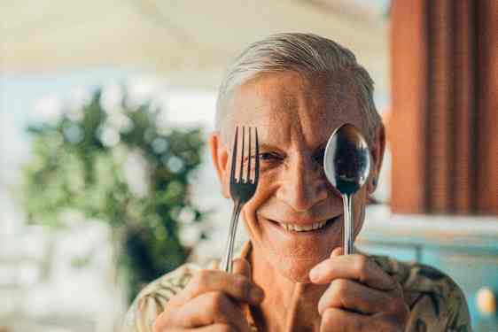 Hymyilevä mies pitää haarukkaa ja lusikkaa kasvojensa edessä.