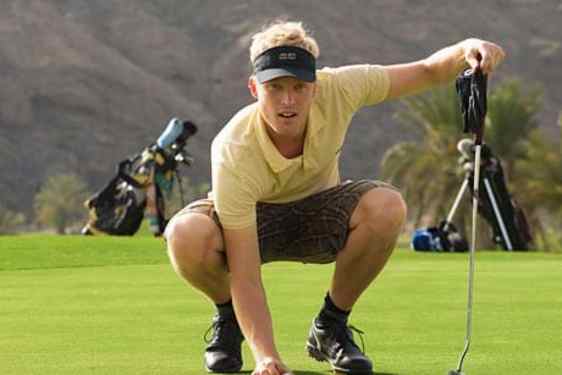 Mies lyömässä golfkentällä