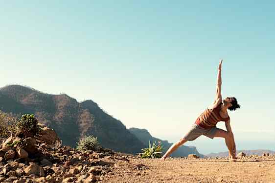 Mies joogaamassa, taustalla vuoristomaisema.