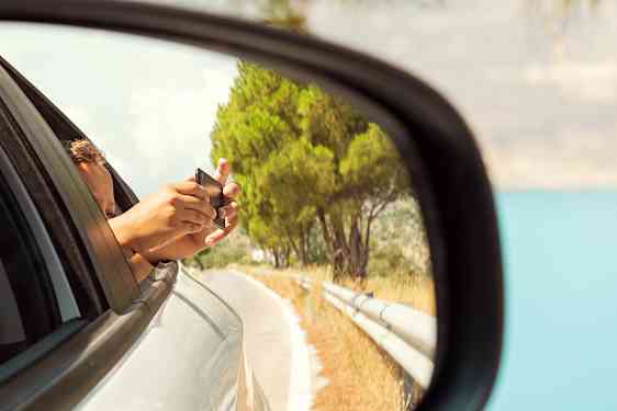 Auton sivupeilissä näkyy takaikkunasta ulos kurkottava henkilö, joka kuvaa puhelimellaan.