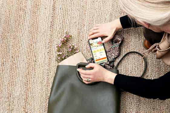 Nainen laittaa puhelimen, jossa Tjäreborgin sovellus auki, kassiinsa.