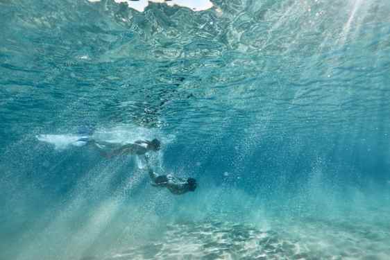 Mies ja nainen sukeltavat pinnan alla.