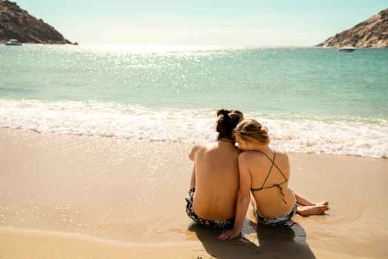 Pariskunta istuu hiekkarannalla aivan vesirajassa.