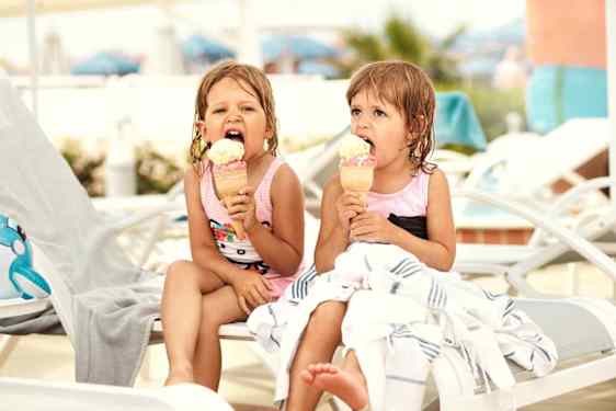Pienet tytöt syömässä jäätelöä uimapuvut päällä aurinkotuolissa.