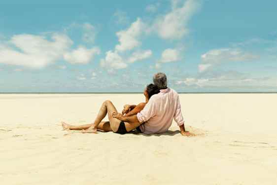 Pariskunta hiekkarannalla pakettimatkalla nojailemassa toisiinsa