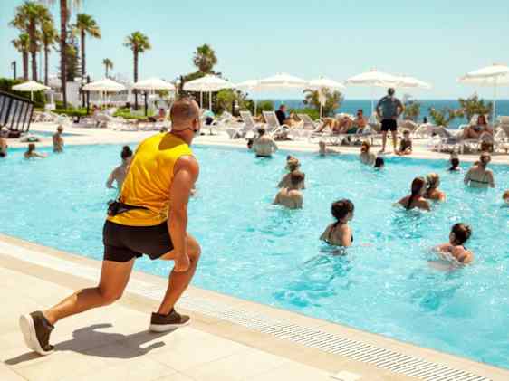 Hotellin kunto-ohjaaja ohjaamassa altaan vierellä vesijumppaa altaassa oleville osallistujille.