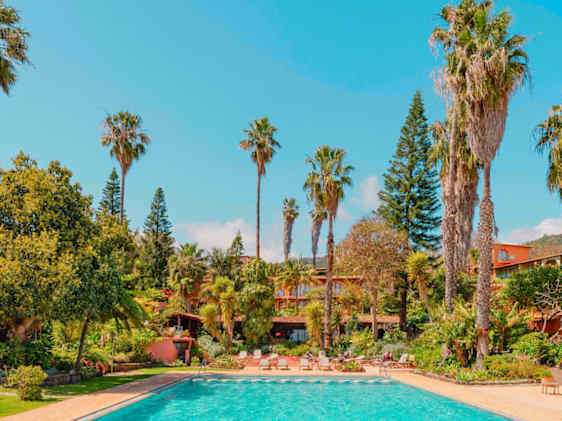 Hotellin allasalue puutarhan keskellä hotellirakennusten pilkahdellessa puiden lomasta.