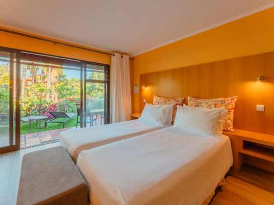Yksiön makuuhuone, jonka ikkunoista näkymä terassille ja hotellin puutarhaan