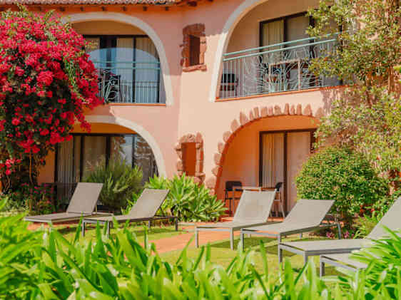 Puutarhan keskellä sijaitsevat hotellihuoneet kohti terassia, jolla muutamia aurinkopetejä