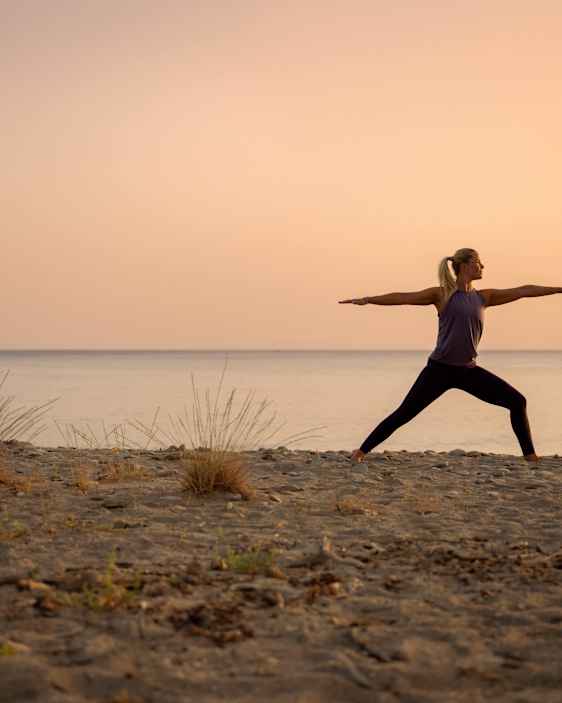 nainen joogaamassa rannalla auringonlaskussa