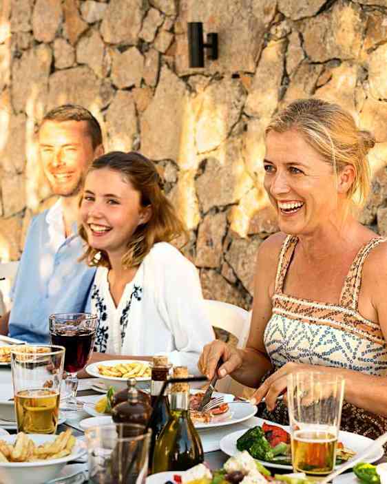 Aikuisia ja lapsia ruokailemassa ja keskustelemassa pöydässä.