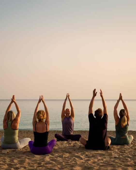 Joogaryhmä rannalla auringonlaskussa